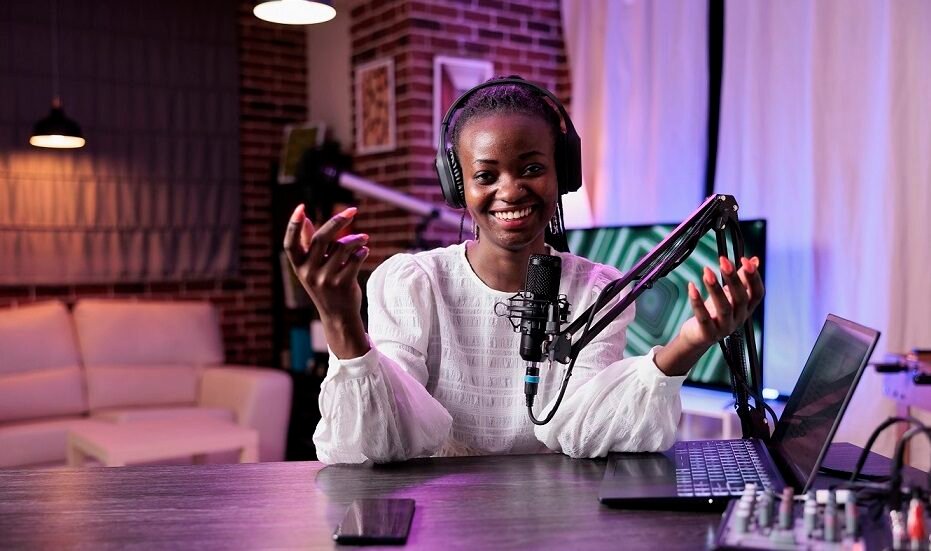 POV of female presenter greeting people on channel podcast, using camera and recording equipment in studio.